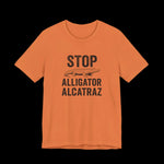 Orange t-shirt with black text and alligator graphic that says "Stop Alligator Alcatraz" on a black background