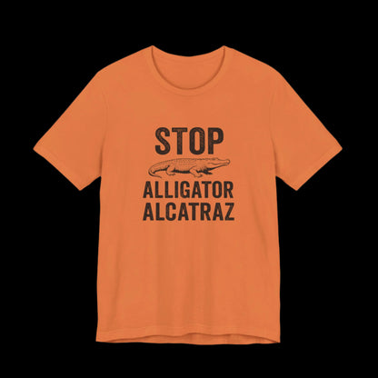 Orange t-shirt with black text and alligator graphic that says "Stop Alligator Alcatraz" on a black background
