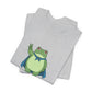 Folded gray t-shirt with a bold graphic of the Portland protest frog—red eyes, blue cape, and unimpressed face by empowHERbyHeidi