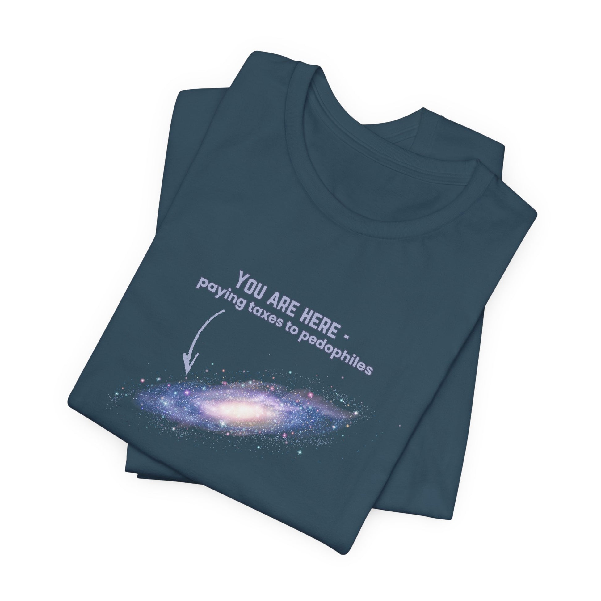 Folded dark blue t-shirt with graphic of the Milky Way galaxy with an arrow pointing to it and text that says "YOU ARE HERE - Paying taxes to pedophiles" by empowHER by Heidi