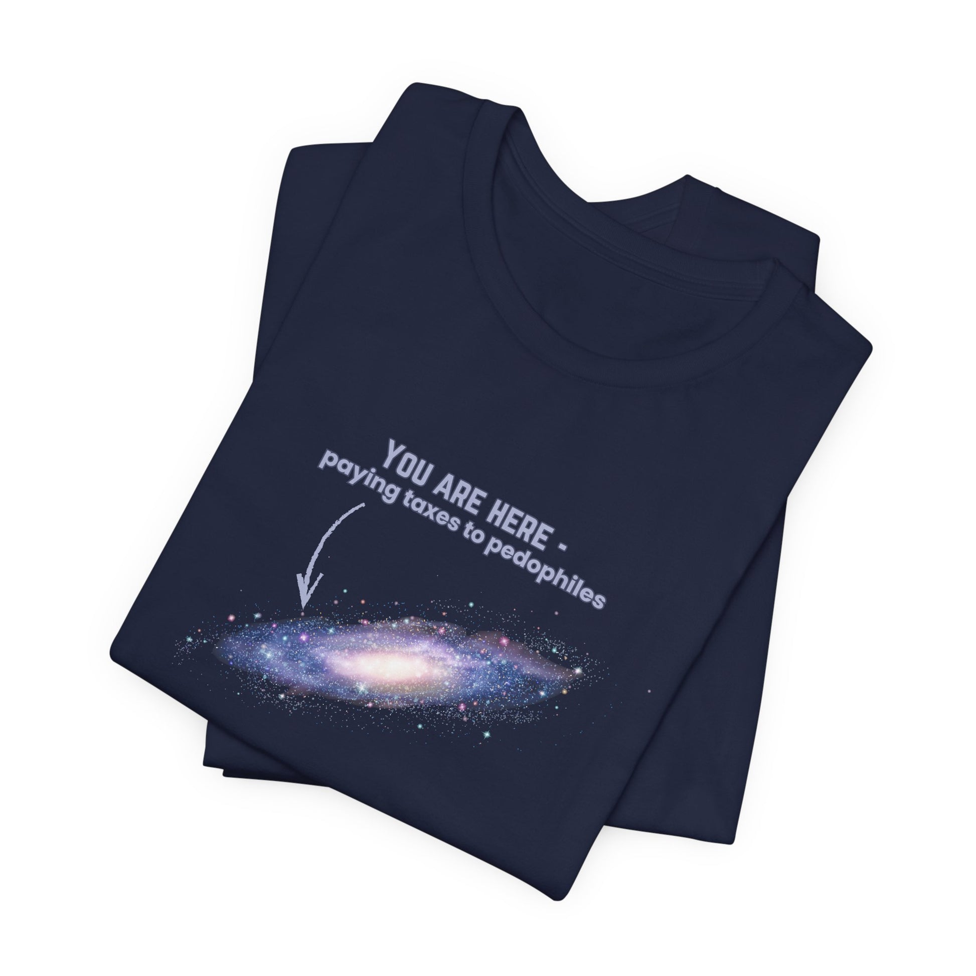 Folded navy blue t-shirt with graphic of the Milky Way galaxy with an arrow pointing to it and text that says "YOU ARE HERE - Paying taxes to pedophiles" by empowHER by Heidi