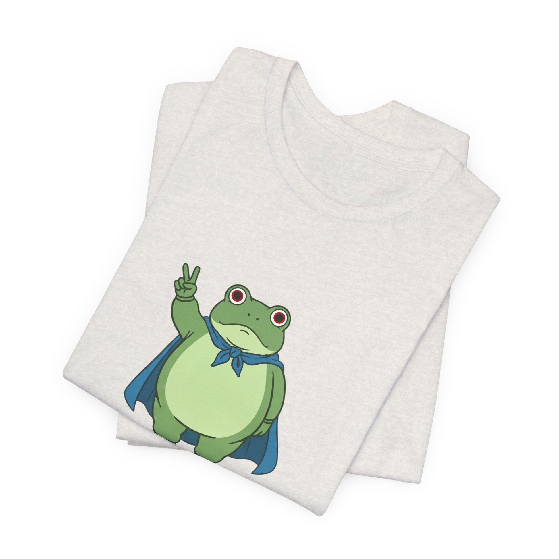 Folded heather cement t-shirt with a bold graphic of the Portland protest frog—red eyes, blue cape, and unimpressed face by empowHERbyHeidi