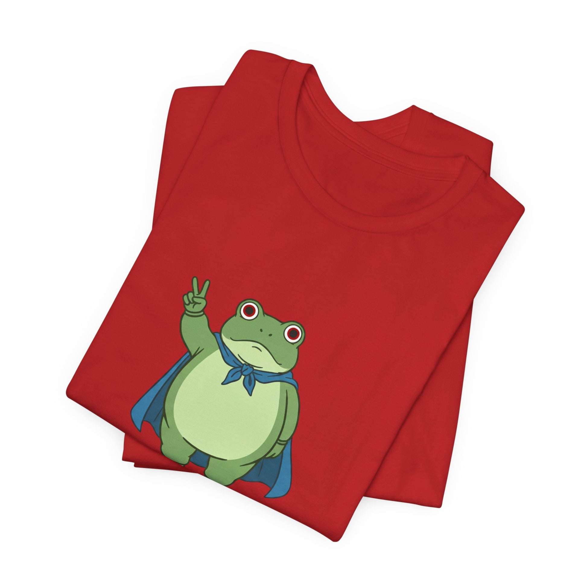 Folded red t-shirt with a bold graphic of the Portland protest frog—red eyes, blue cape, and unimpressed face by empowHERbyHeidi