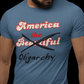 Stone blue t-shirt with the saying "america the beautiful" but "beautiful" is crossed out and replaced with the word "oligarchy"