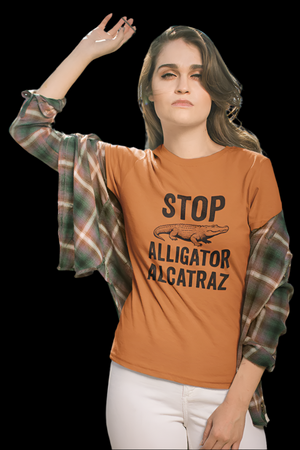 Woman wearing an orange t-shirt with black text that says "STOP ALLIGATOR ALCATRAZ" with an alligator, standing in front of a chain-link fence.